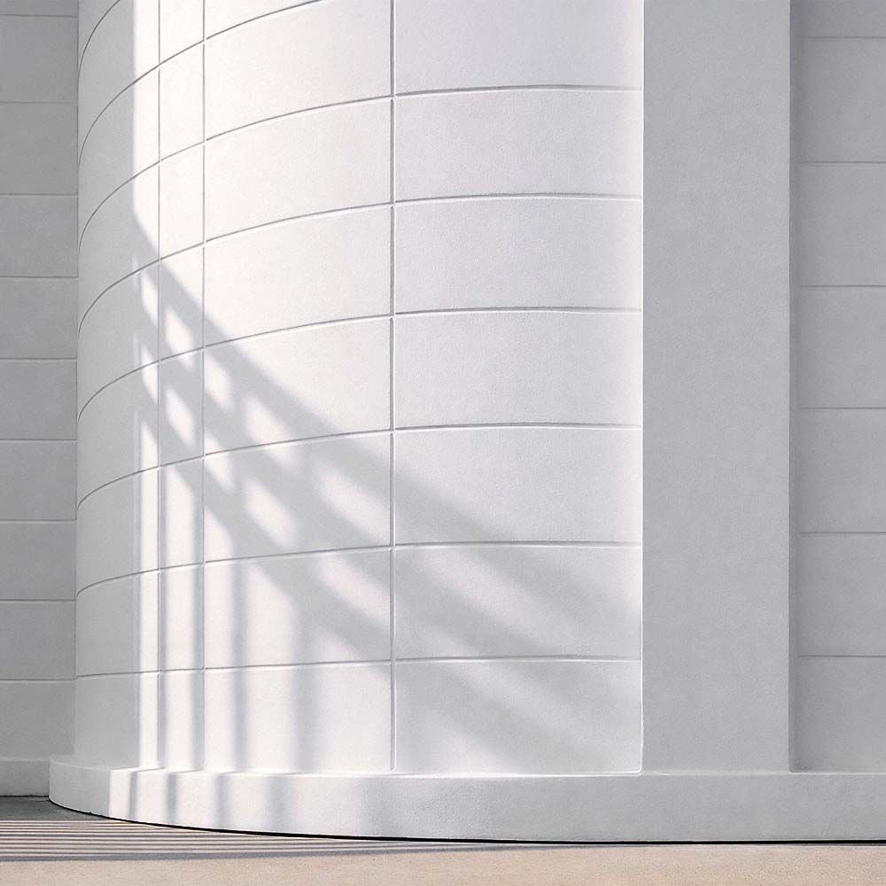 White curved wall with rectangular tiles, casting shadows on a light-colored floor.