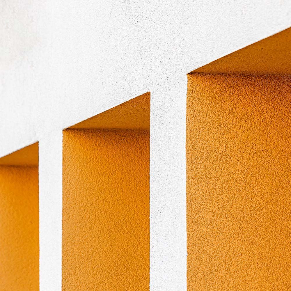 Modern architectural detail with white stucco wall and recessed orange geometric openings