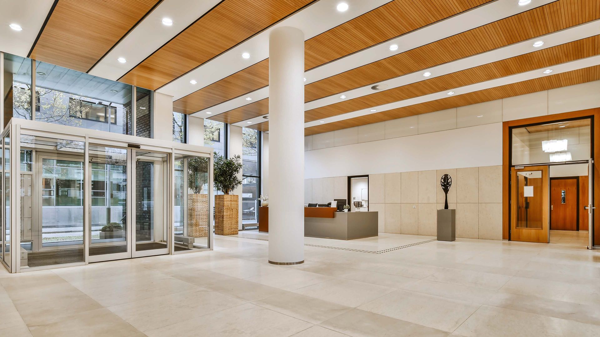 Modern office lobby with revolving doors, reception desk, and wood panel ceiling.