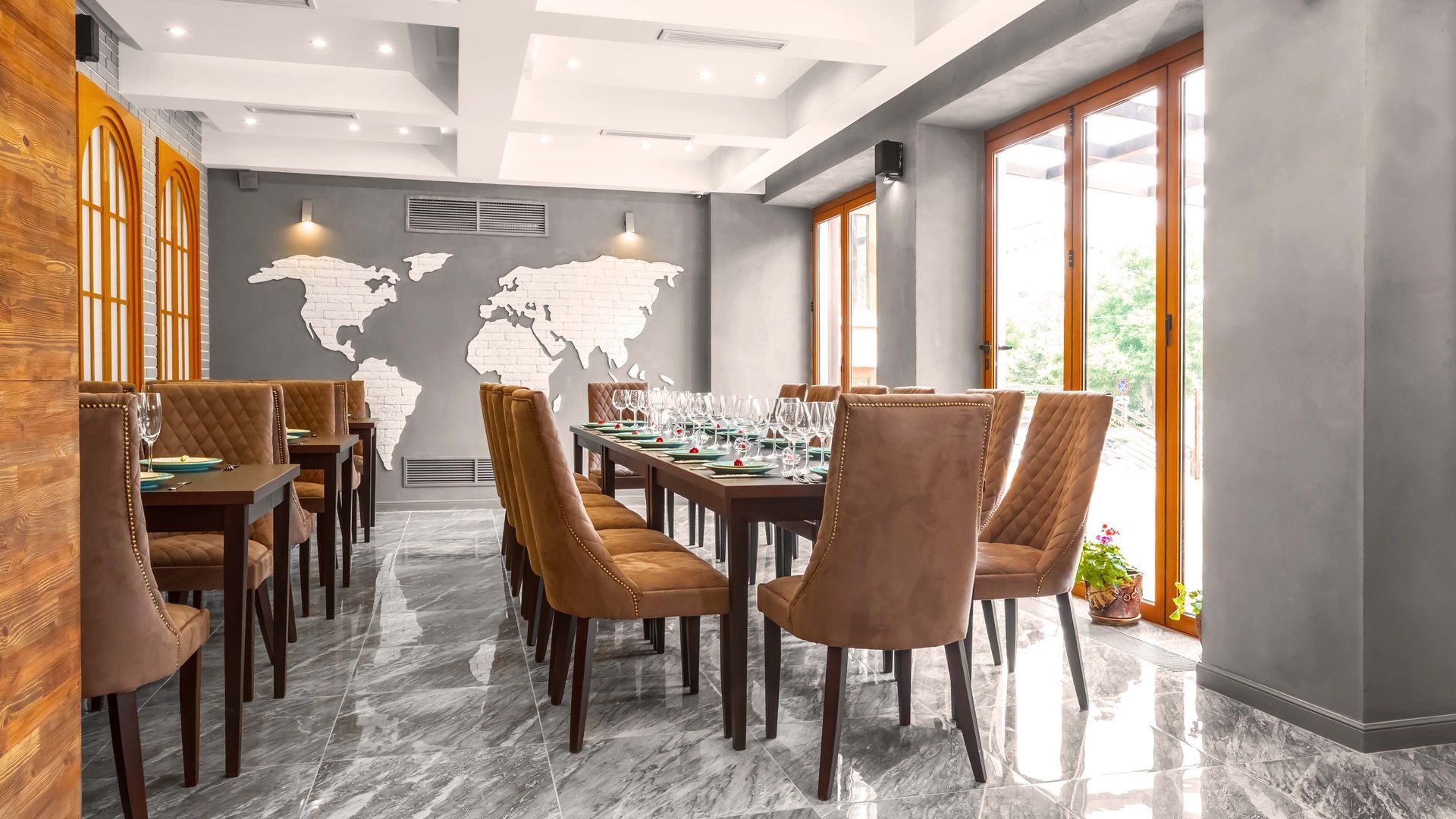 Restaurant dining area with tables, chairs, world map on wall, and large windows.