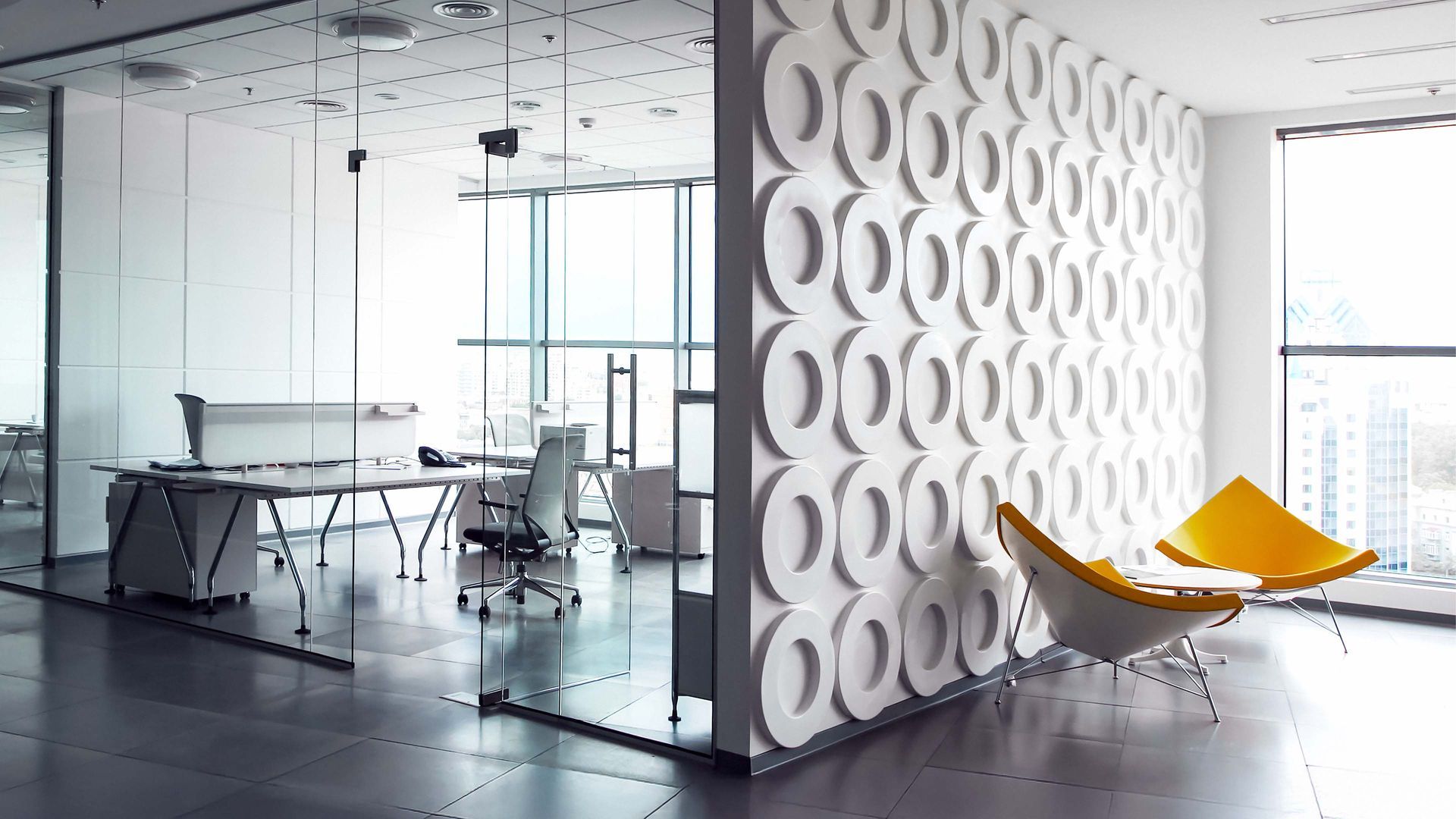 Modern office space with glass walls, patterned accent wall, and a yellow lounge chair.