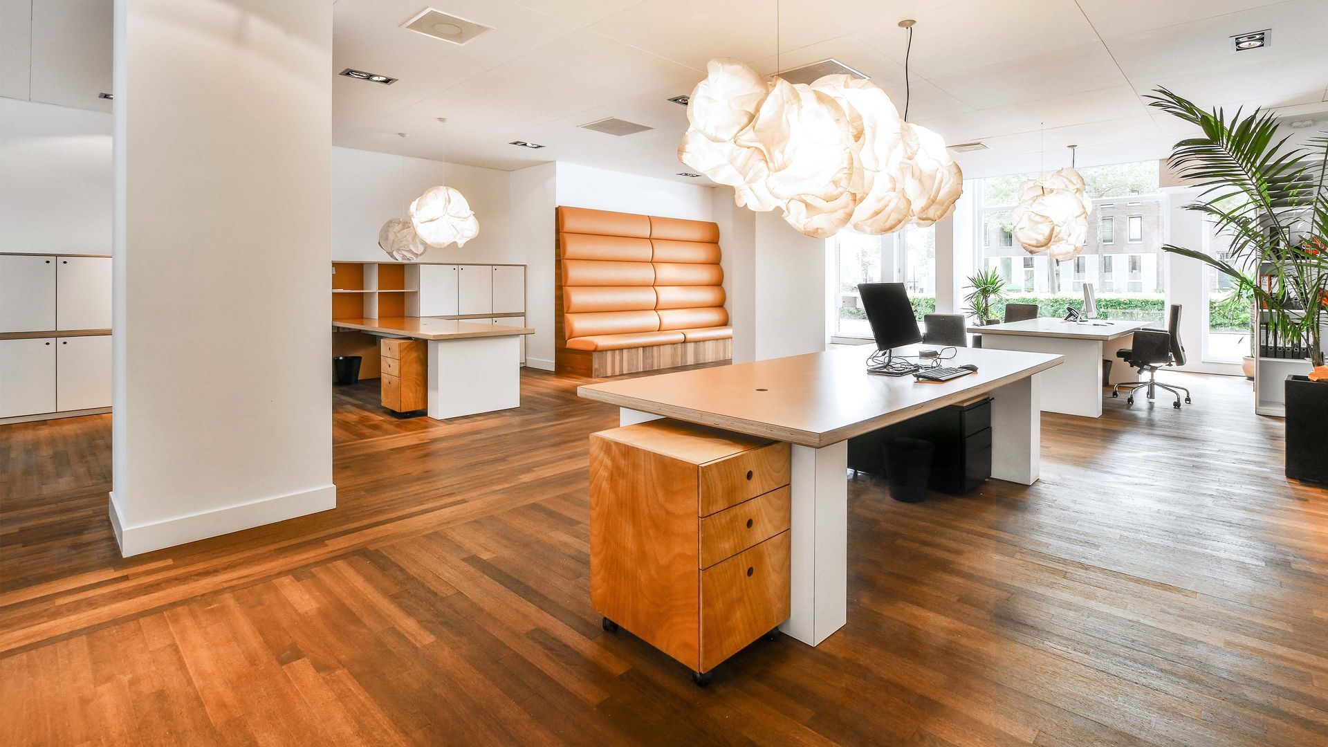 Modern office interior with wooden floors, desks, and decorative cloud-shaped lights.