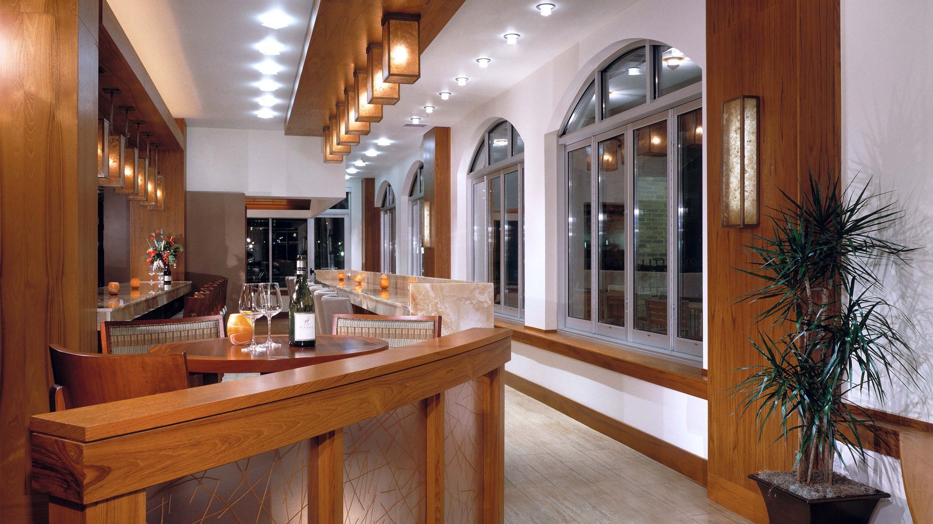 Interior of a bar with wooden accents, arched windows, and a plant.