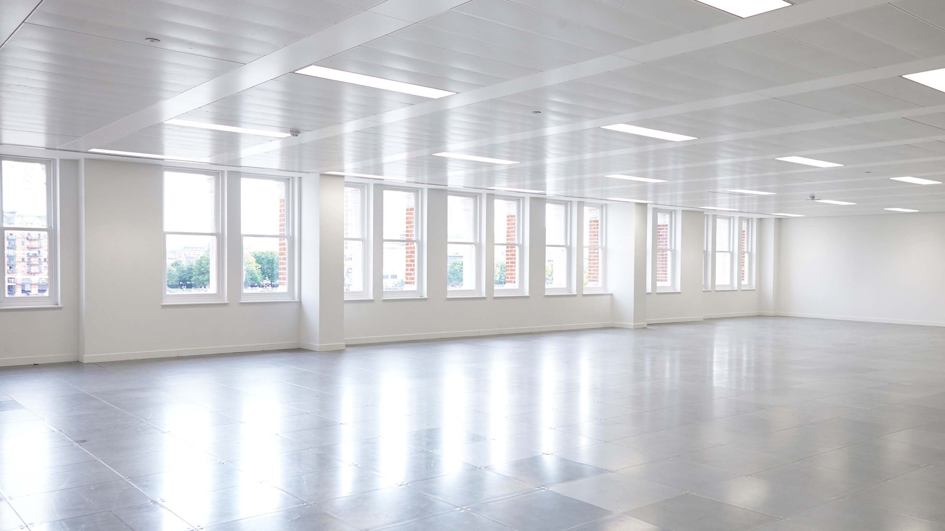 Empty, bright, modern office space with many windows along a white wall and a reflective floor.