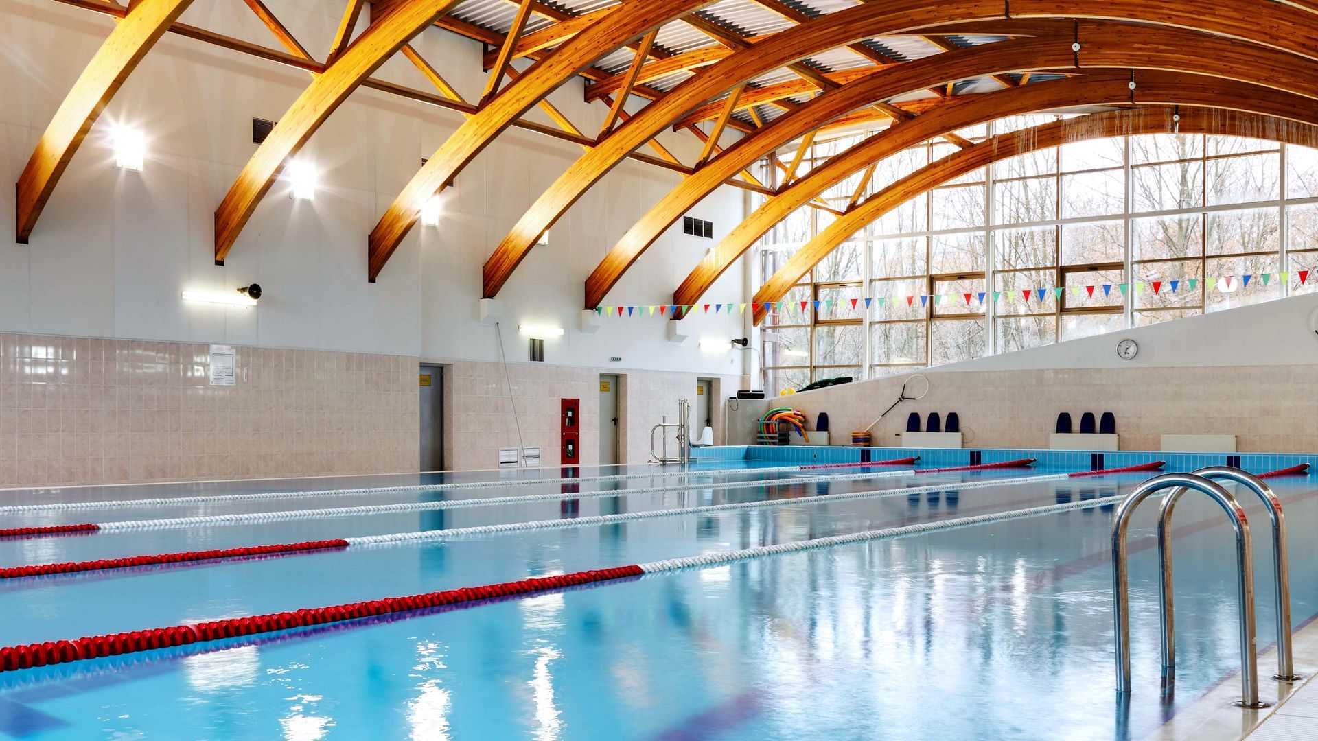 Indoor swimming pool with arched wooden ceiling, marked lanes, and large windows.
