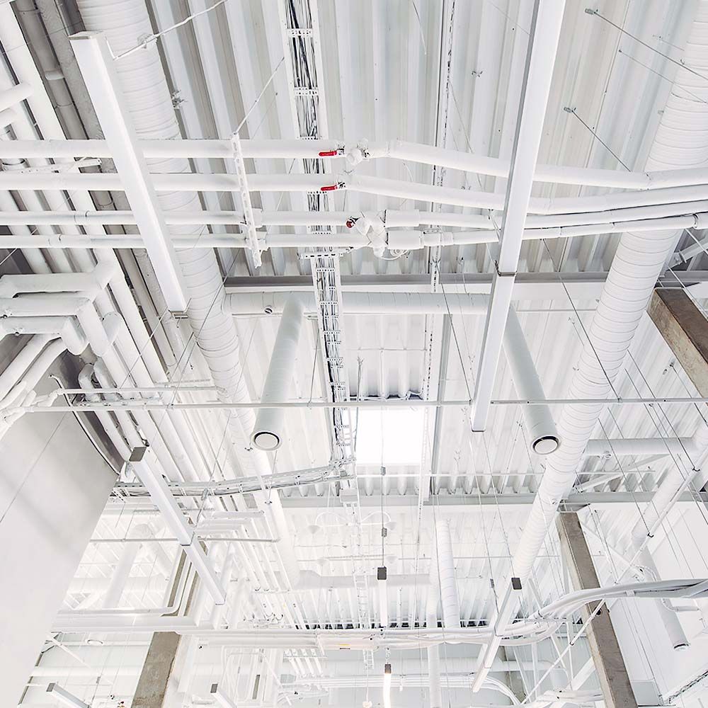 White ceiling with exposed pipes, ducts, and lighting fixtures.