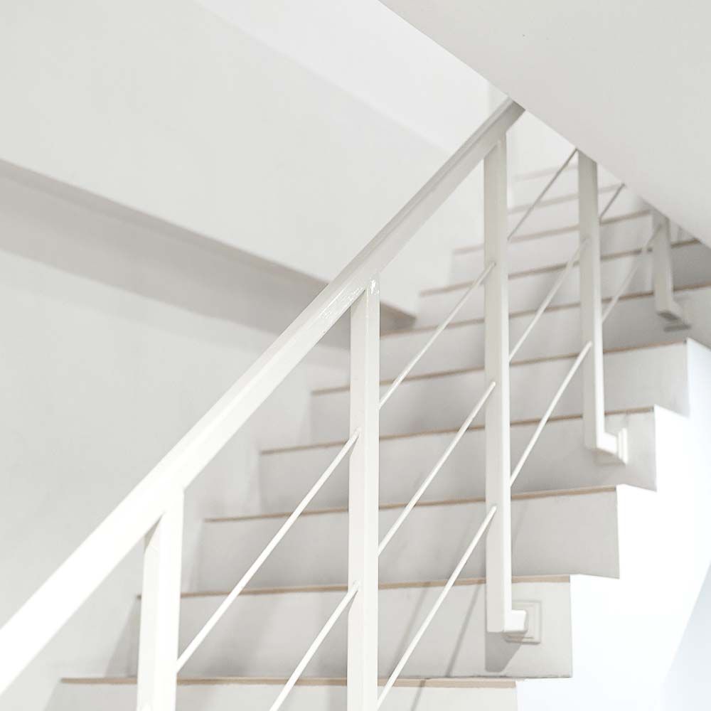 White staircase with minimalist metal handrail against a white wall.