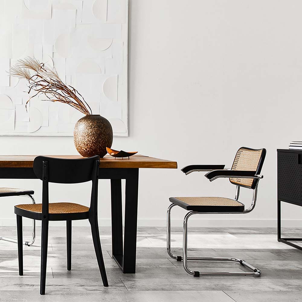 Dining area with wooden table, black and woven chairs, and decorative vase.