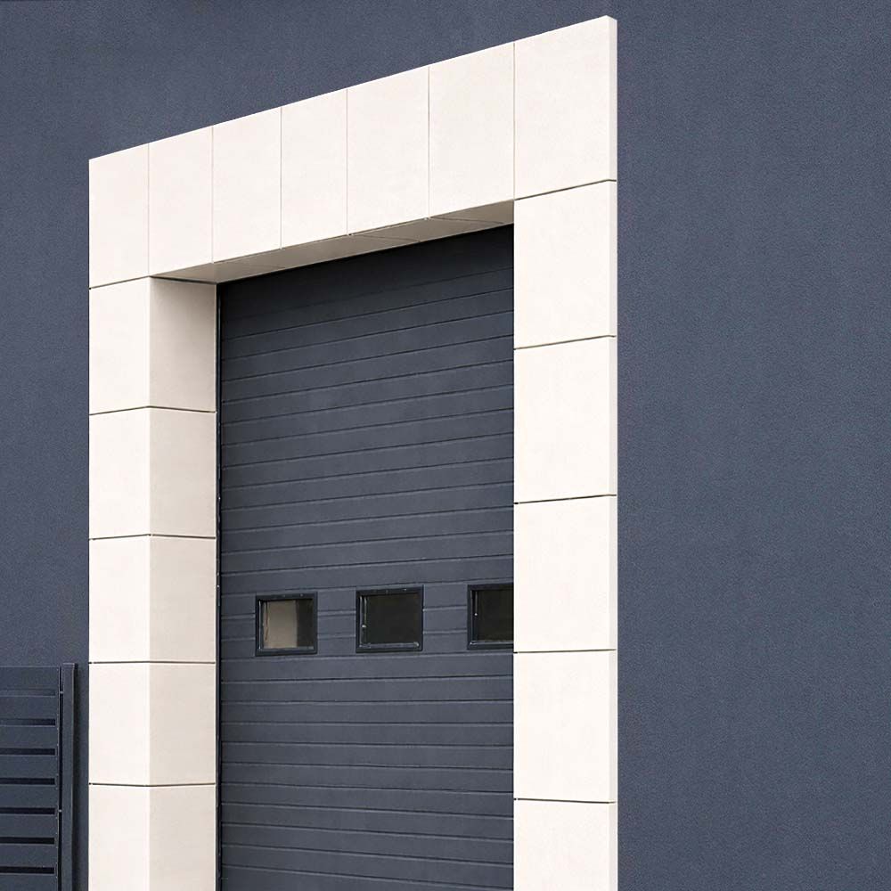 Gray garage door with a white rectangular frame on a blue wall.