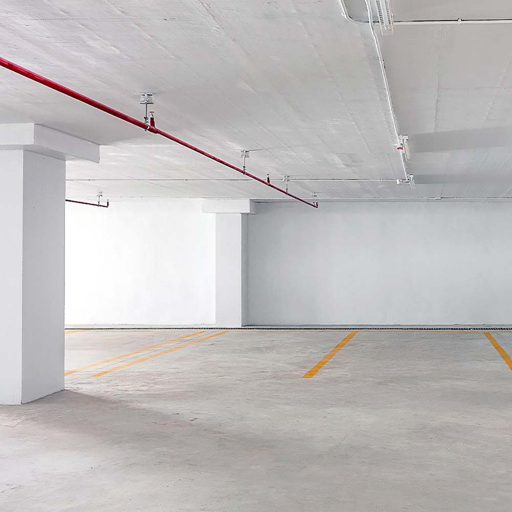 Empty, white concrete parking garage with yellow parking space lines and red pipes on the ceiling.