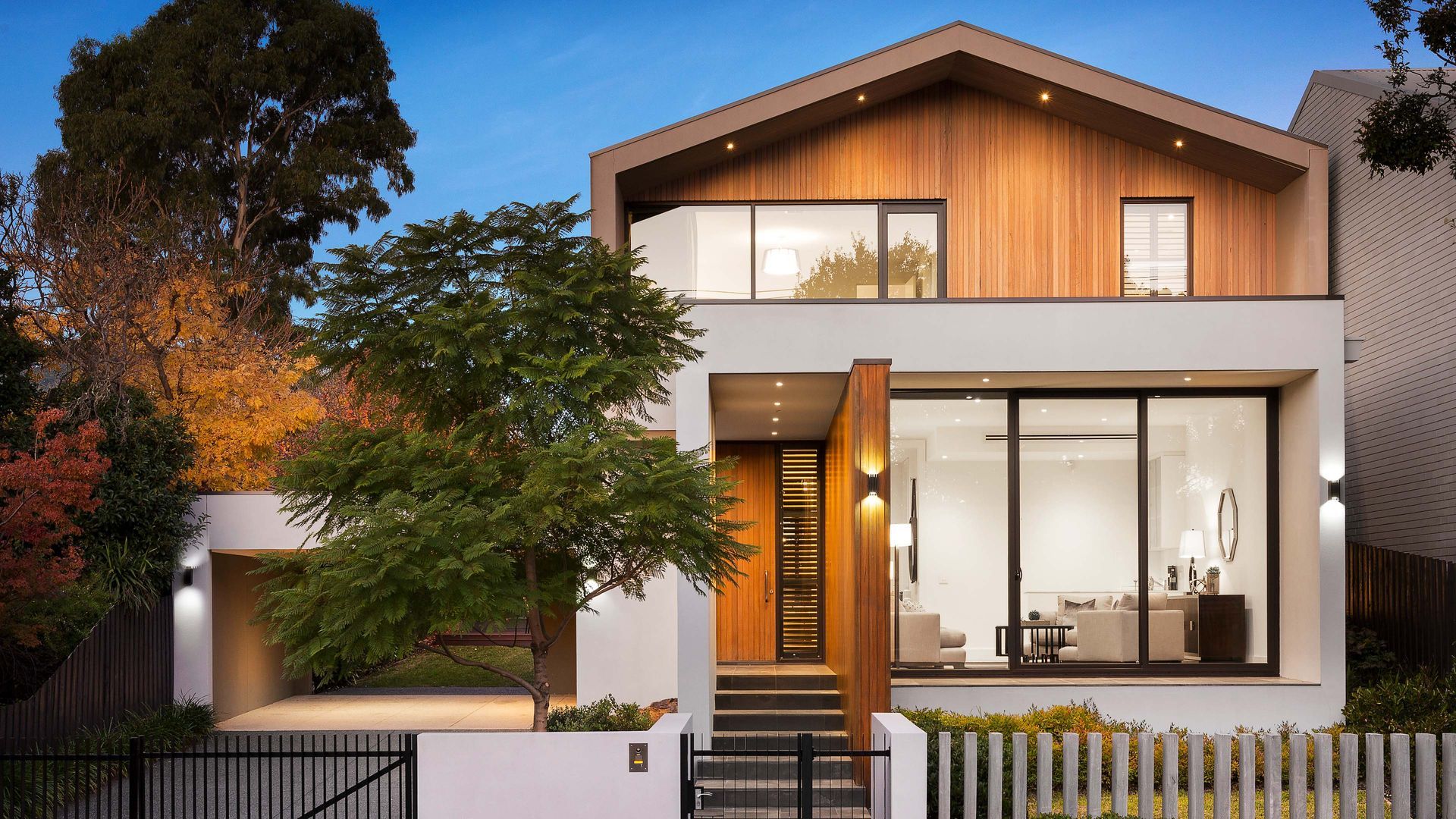 Modern two-story house with white facade, wooden accents, large windows, and landscaped yard.