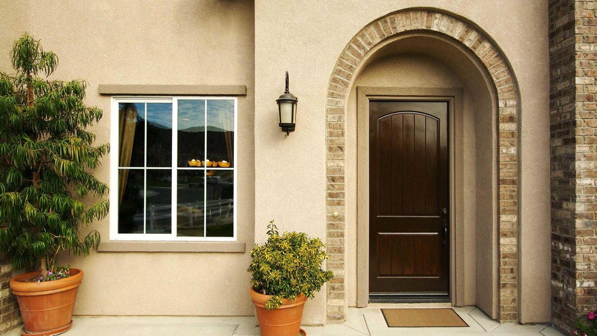 Beige stucco house exterior with window, door, and potted plants.