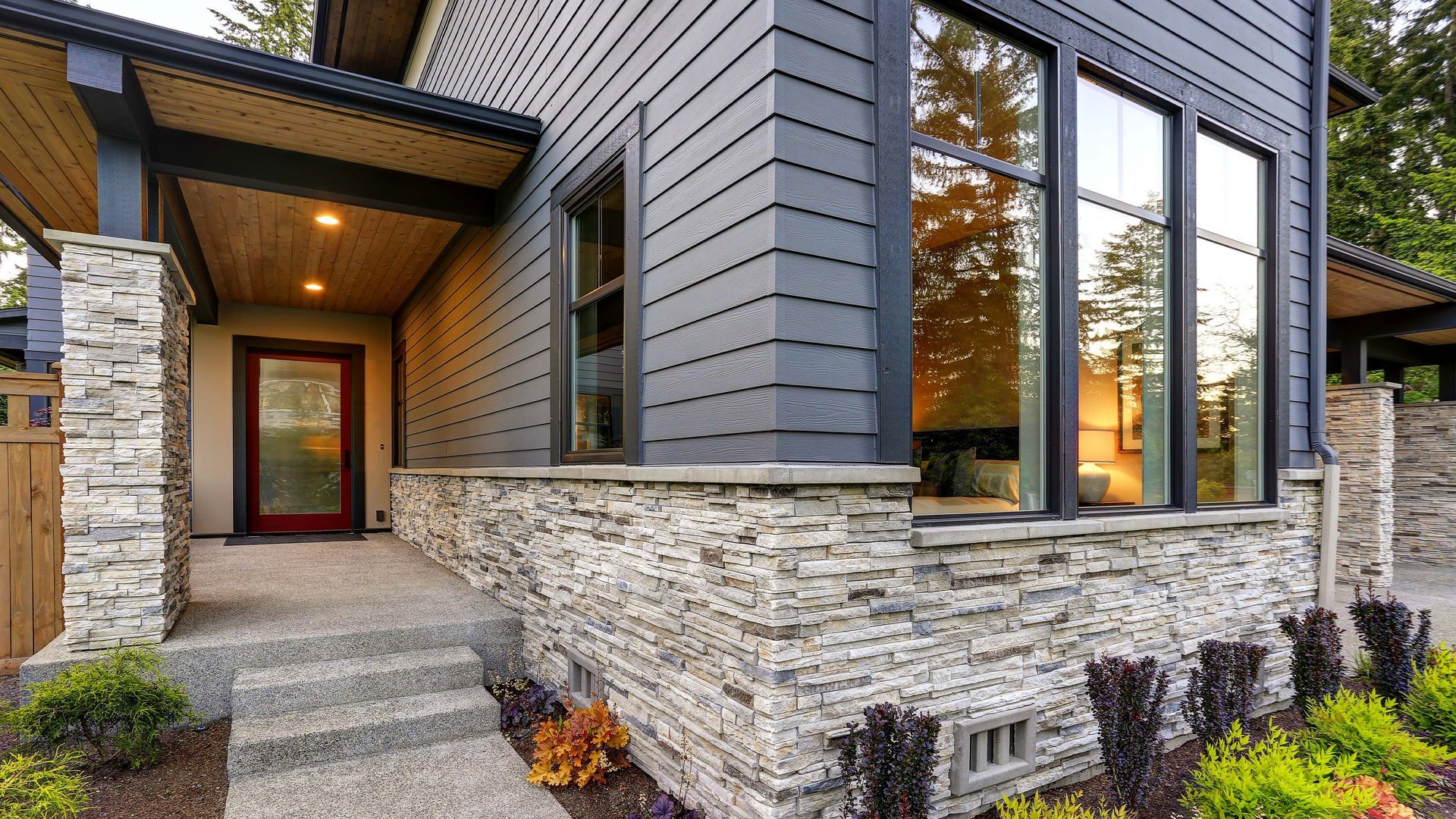 Modern house exterior with gray siding, stone accents, and large windows.