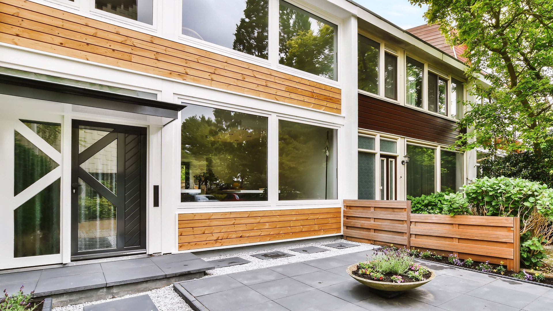Modern house exterior with large windows, wooden accents, and patio.