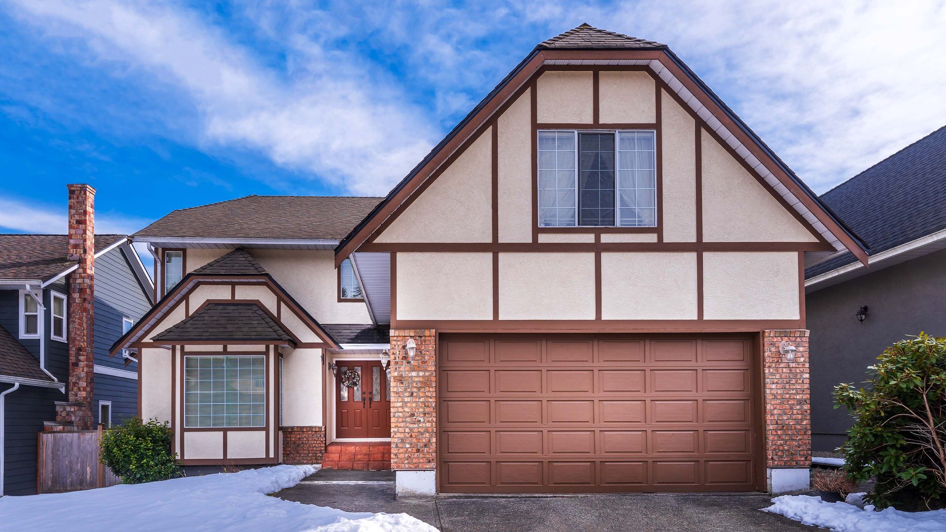 Two-story house with brown garage door, beige siding, brick accents, and snow-covered ground.