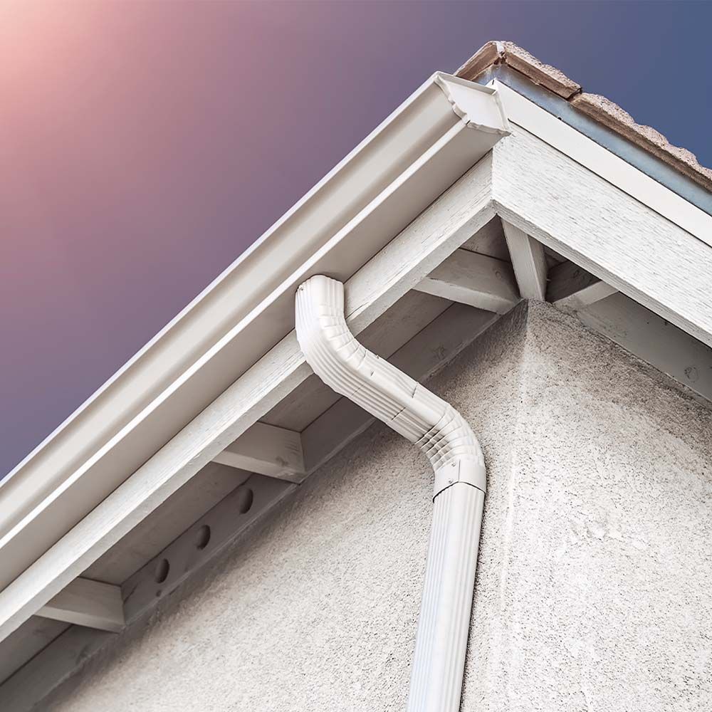 Beige rain gutter and downspout on a stucco-covered house corner.