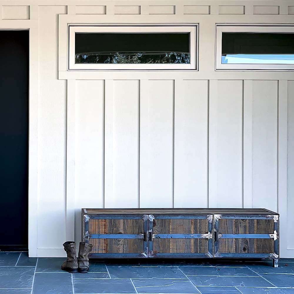 White paneled wall with a rustic wooden cabinet, boots, and windows.