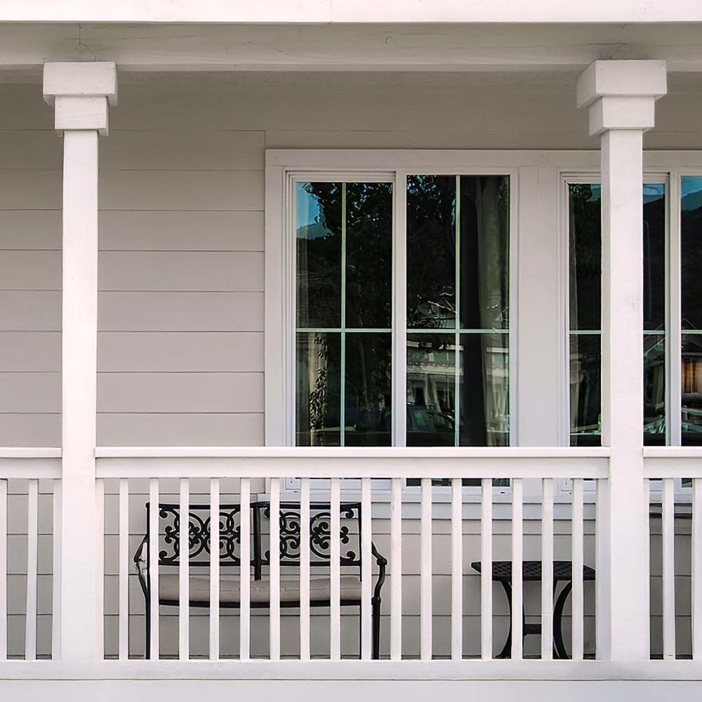 White porch with pillars, railing, and window, with a bench and table.
