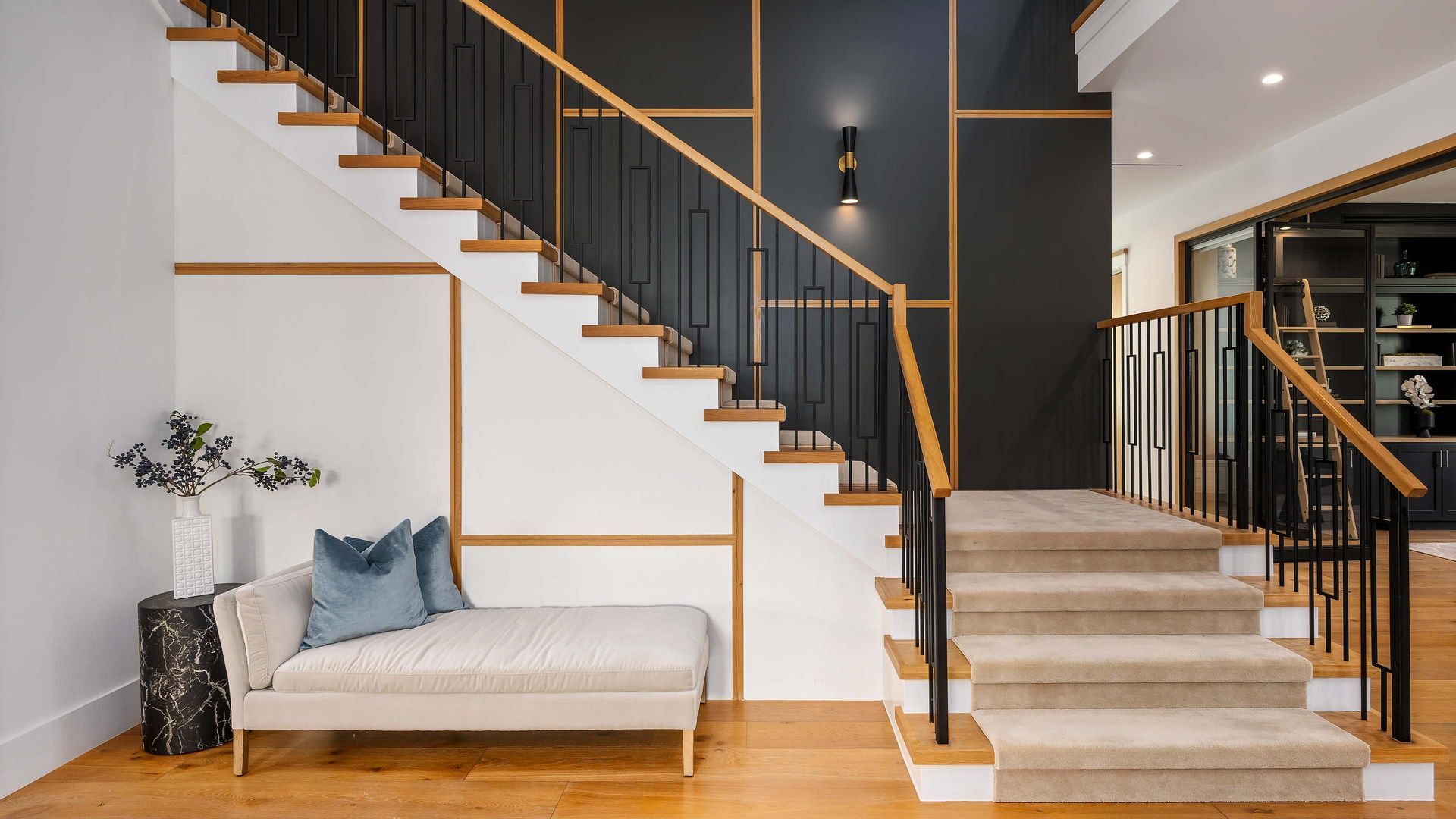 Staircase with wooden steps, black railing, and neutral-colored carpet. A bench and black accent wall are also present.
