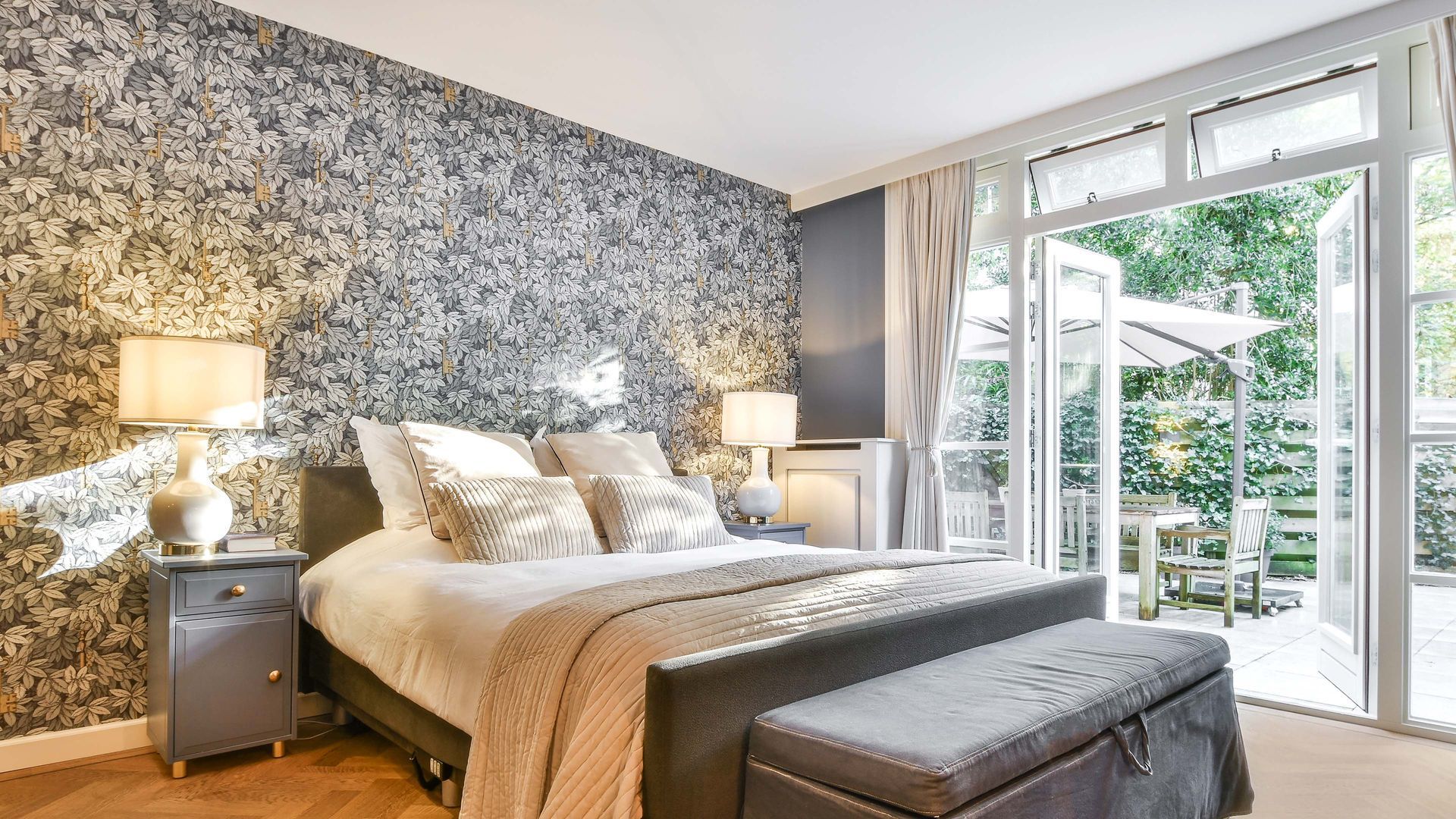 Bedroom with patterned wallpaper, bed, bedside tables with lamps, and doors opening to a patio.
