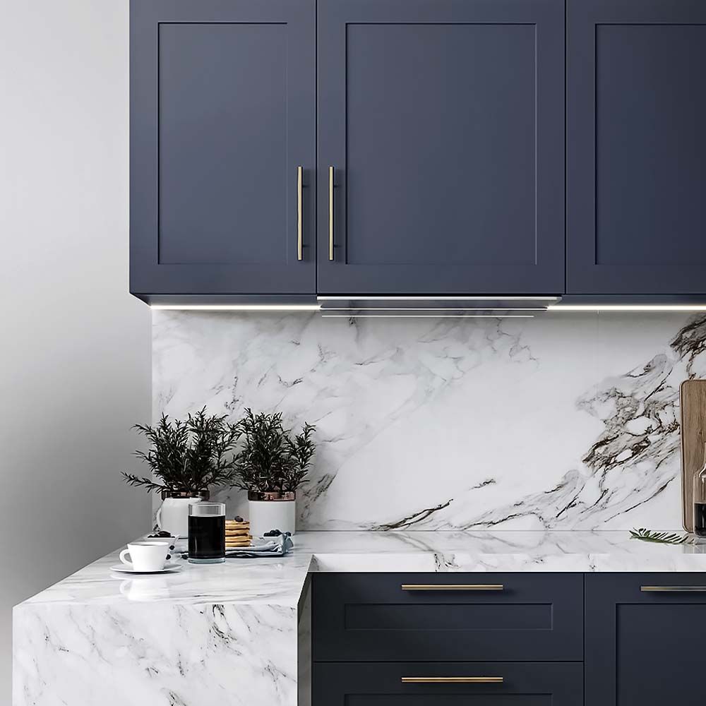 Dark blue kitchen cabinets with marble countertops and backsplash, under-cabinet lighting.