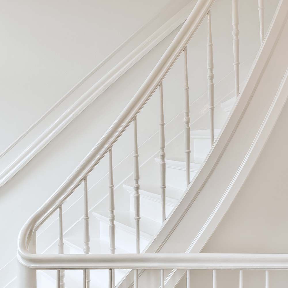 White staircase with banister and balusters against a white wall.