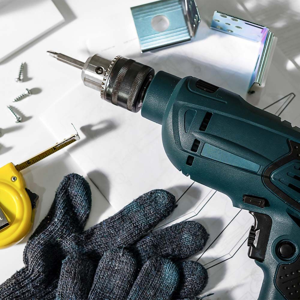 Drill, screws, gloves, and measuring tape on a blueprint, highlighting home repair tools.