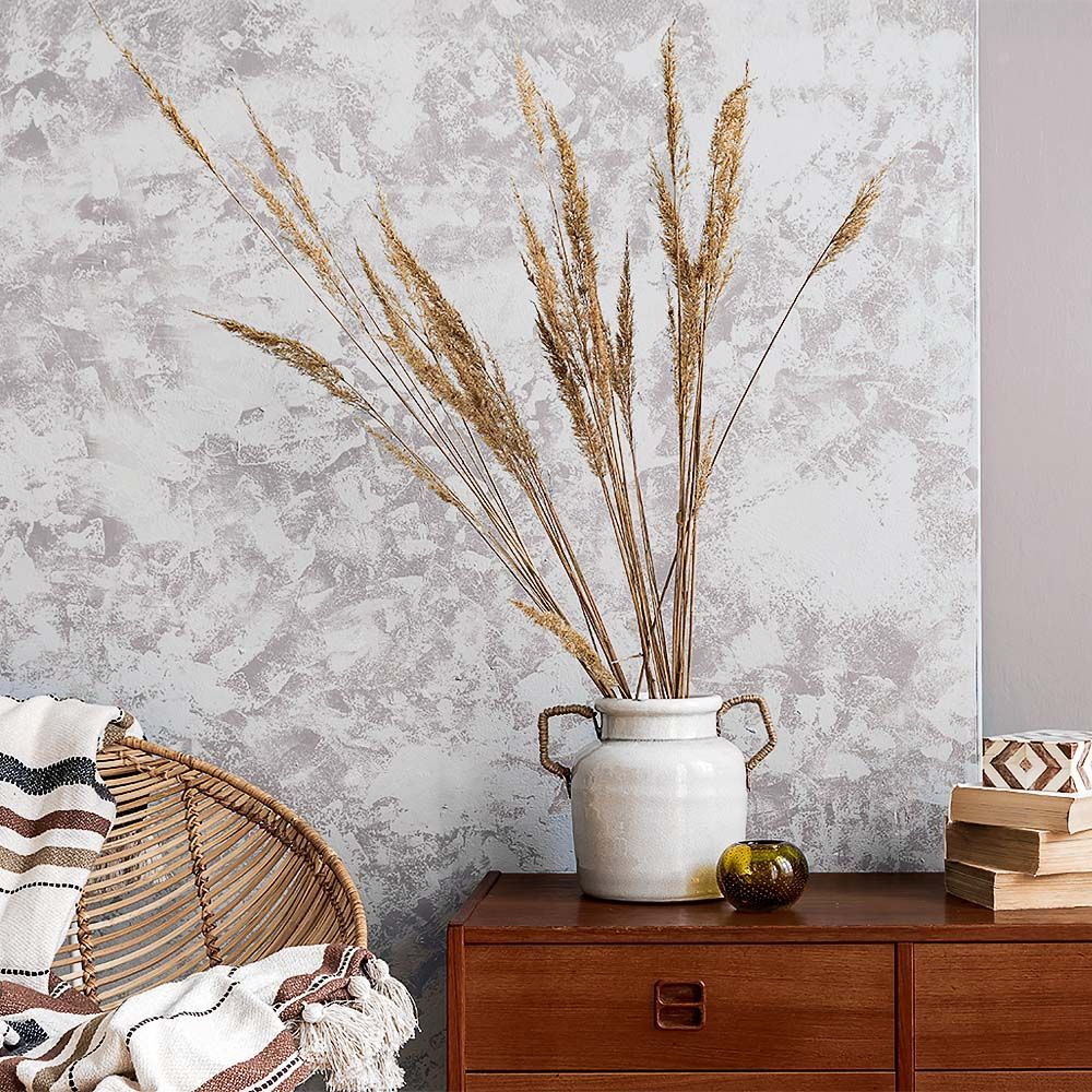 Wicker chair with blanket, vase of dried grasses on a wooden cabinet, against a textured wall.
