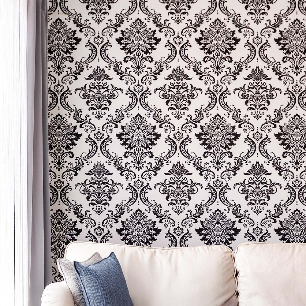 Black and white damask wallpaper behind a white couch with blue pillow. Gray curtain on the left.