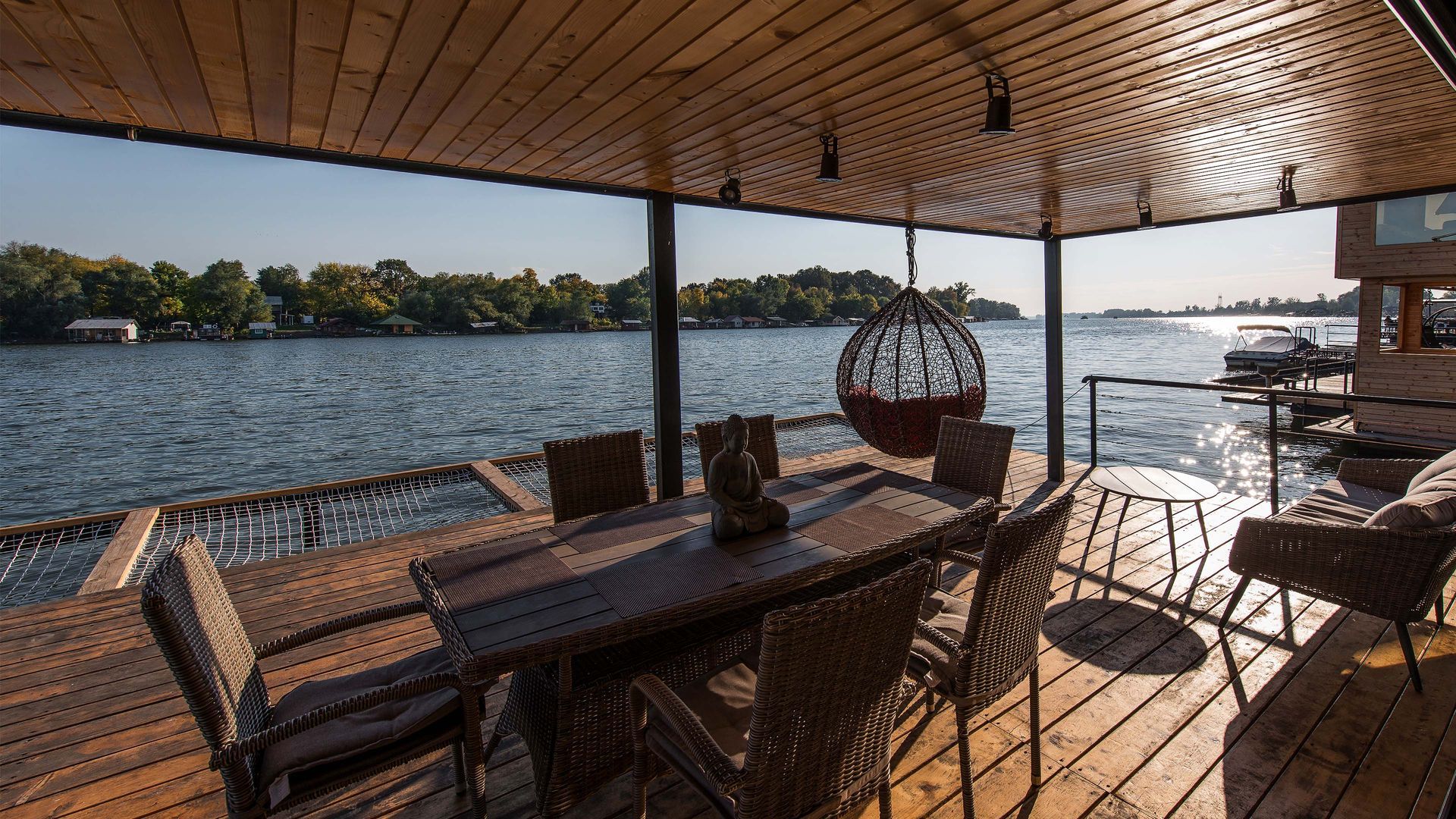 Wooden deck with a table, chairs, and hanging chair overlooking a river.