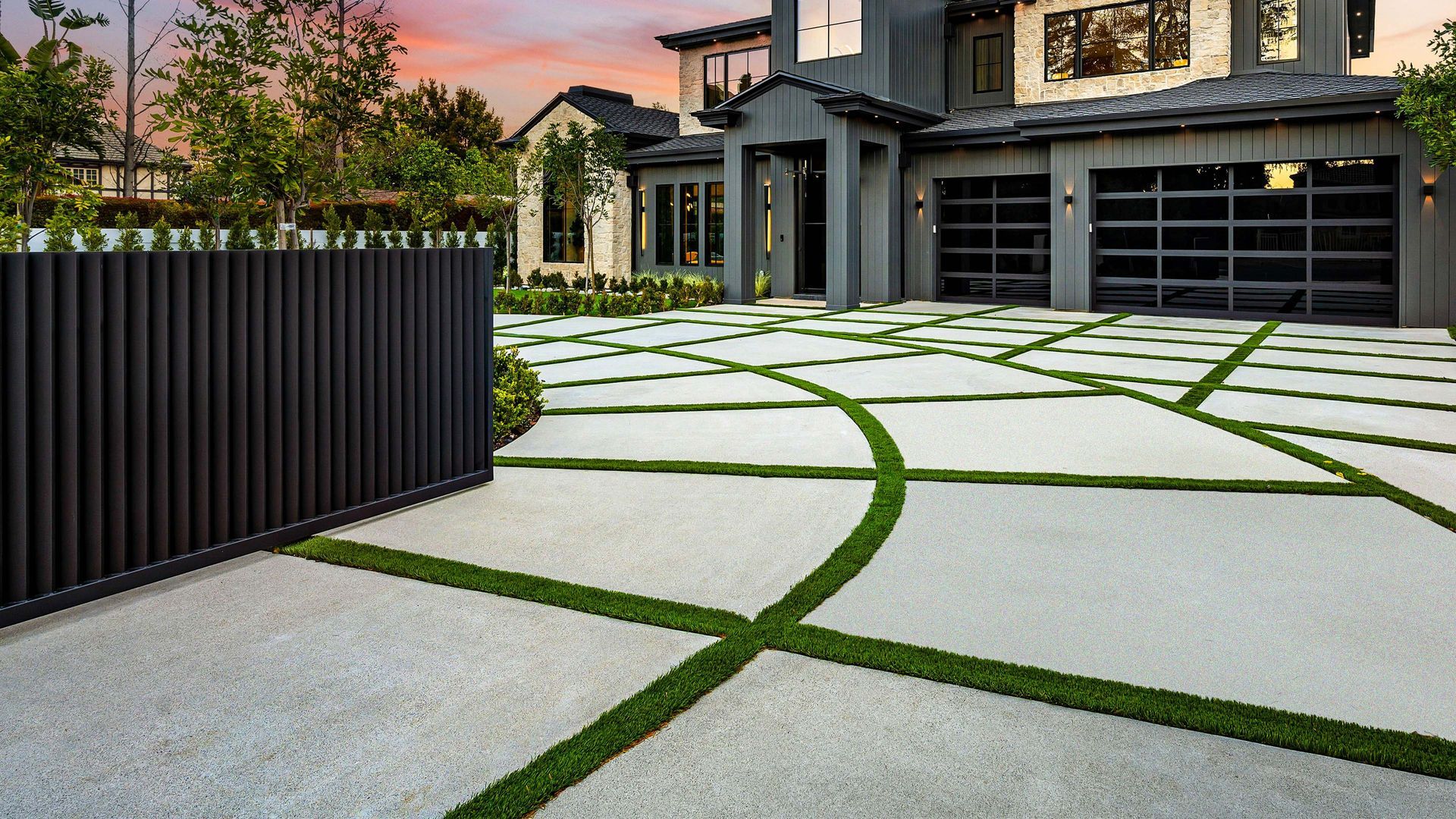 Modern house with concrete driveway featuring green grass accents; a black gate is in the foreground.