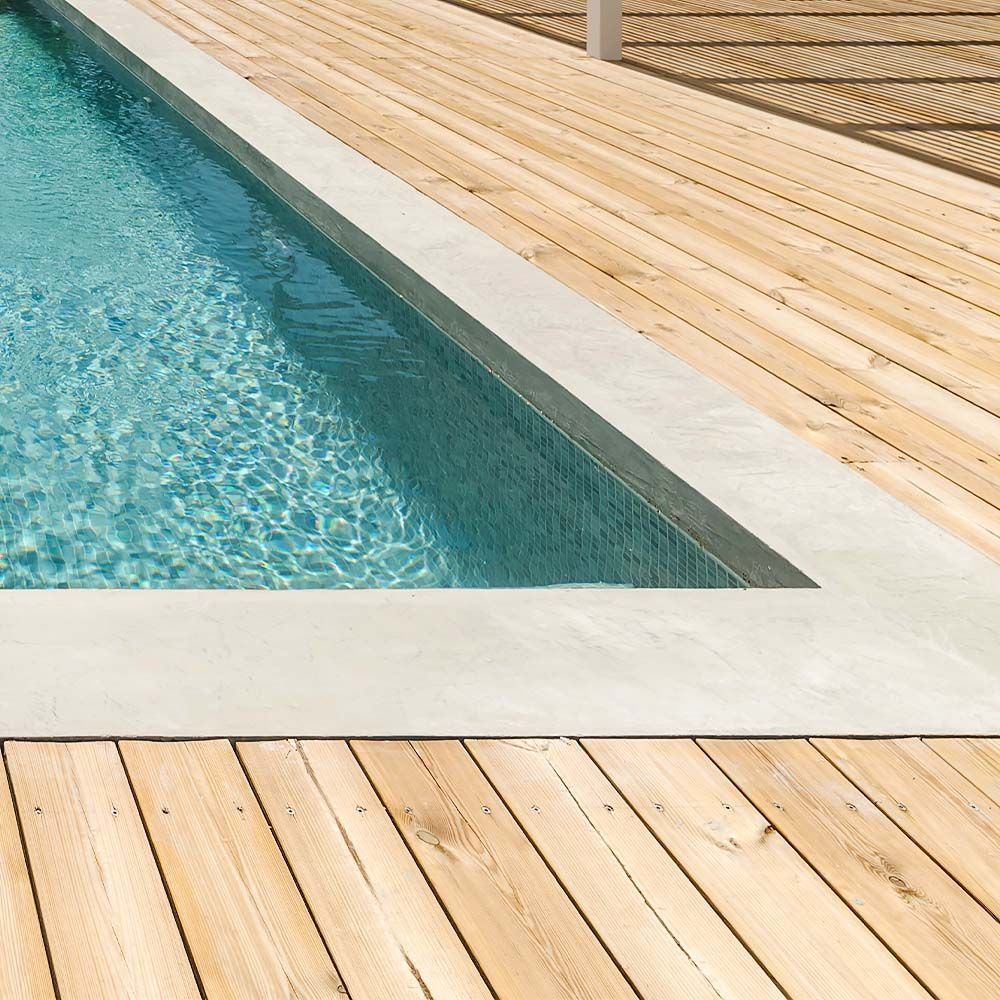 Pool with concrete border next to wooden decking, filled with clear blue water. 