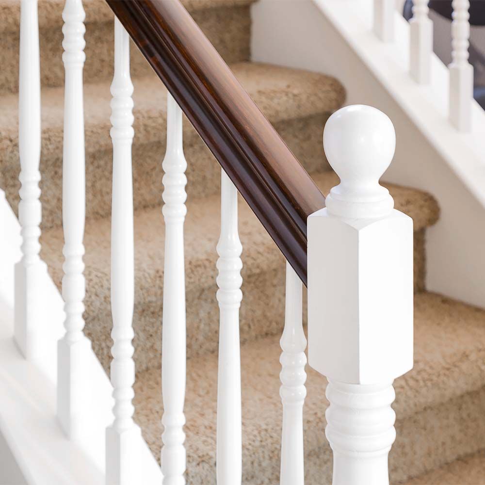 White stair balusters with a dark wood handrail on a carpeted staircase.
