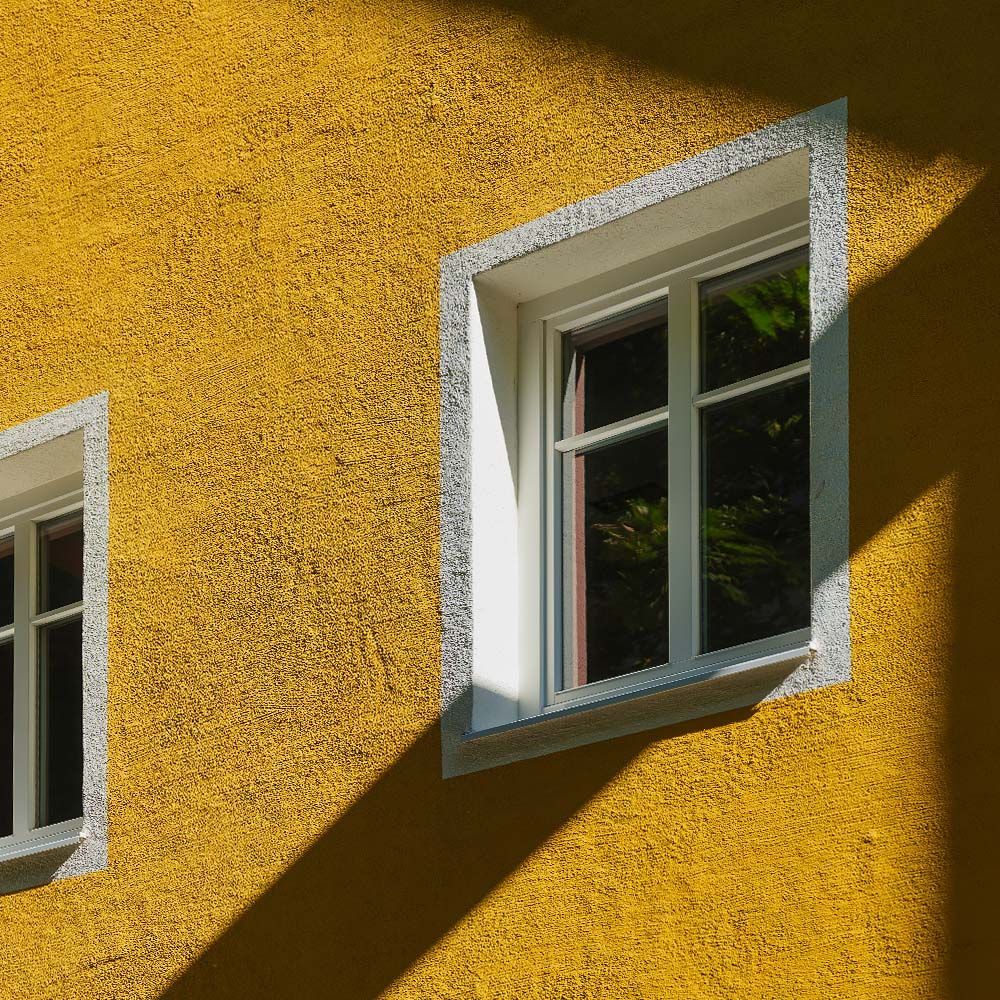 Yellow building exterior with white-framed windows, contrasting shadows.