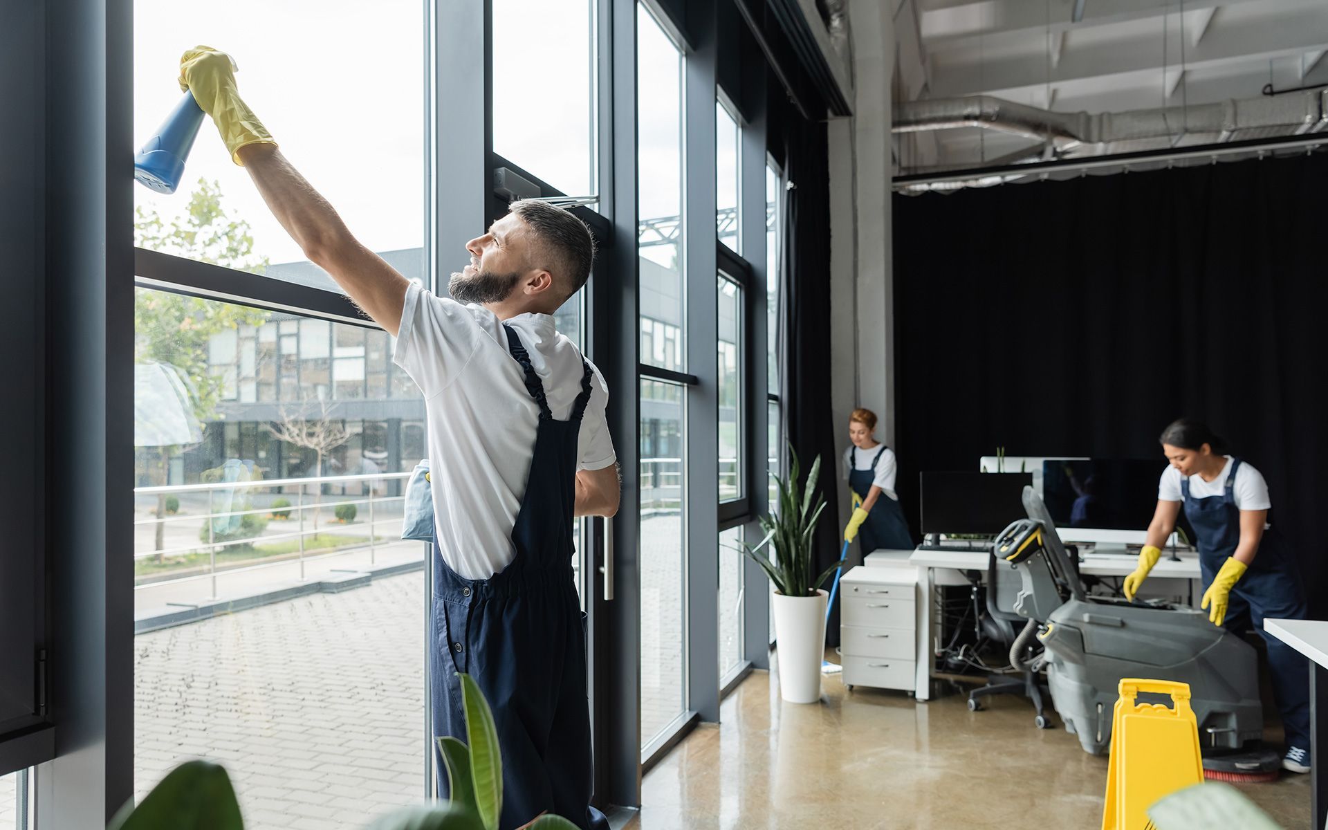 Man cleaning a window, two others cleaning an office.