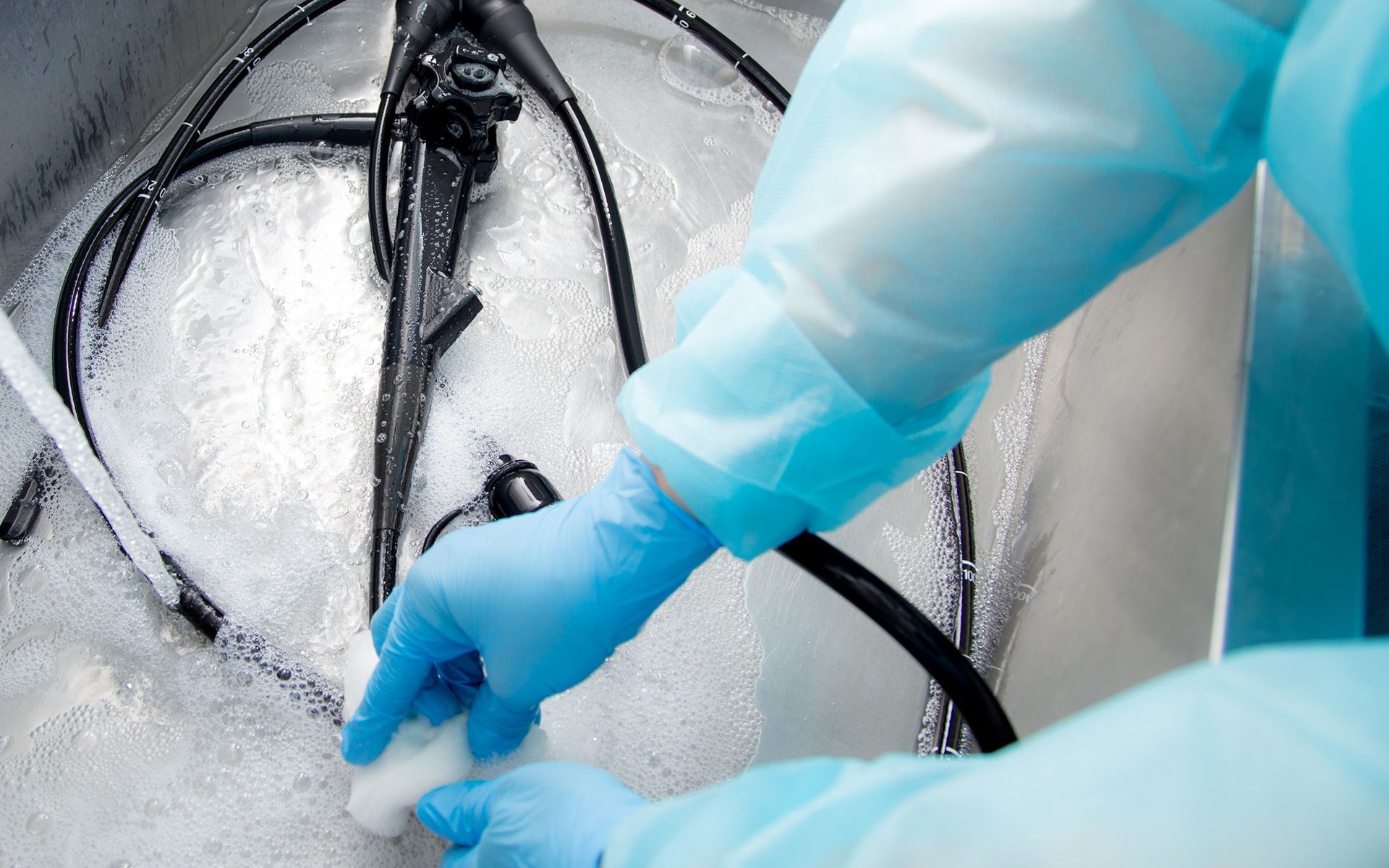 Person in blue gloves cleaning medical equipment in a sink.