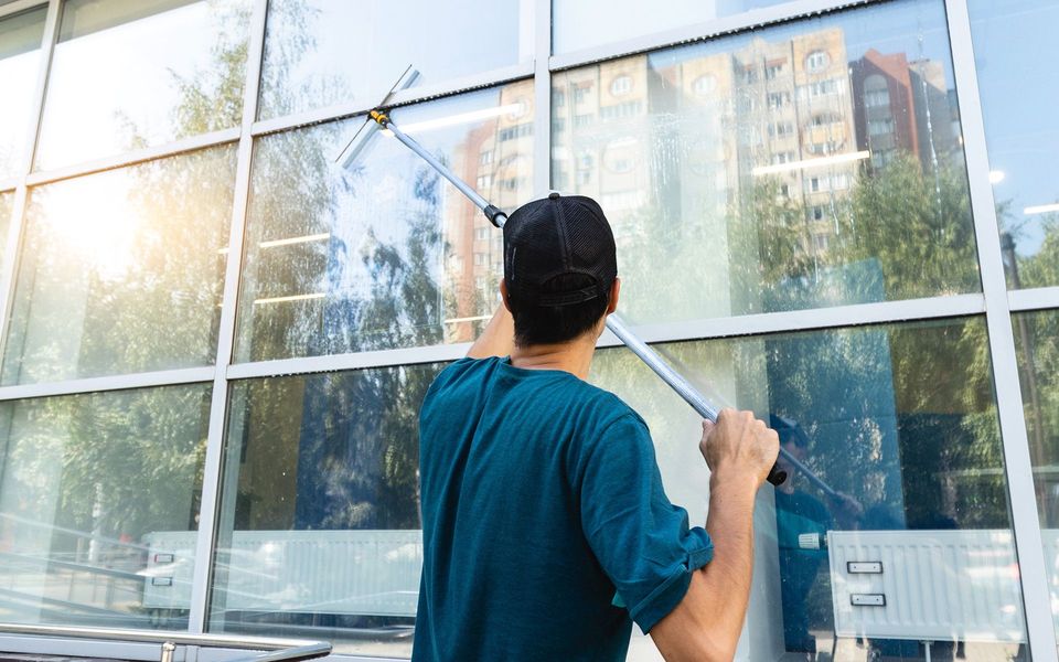 Person cleaning large glass windows with a squeegee outdoors.