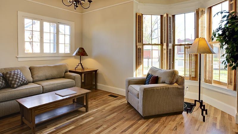 Living room with tan walls, wood floors, couch, armchair, windows, and lamps.