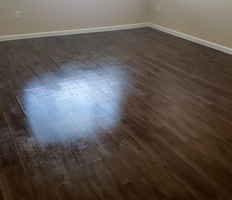 Dark wood-look flooring in a room with beige walls and white trim; light reflections.