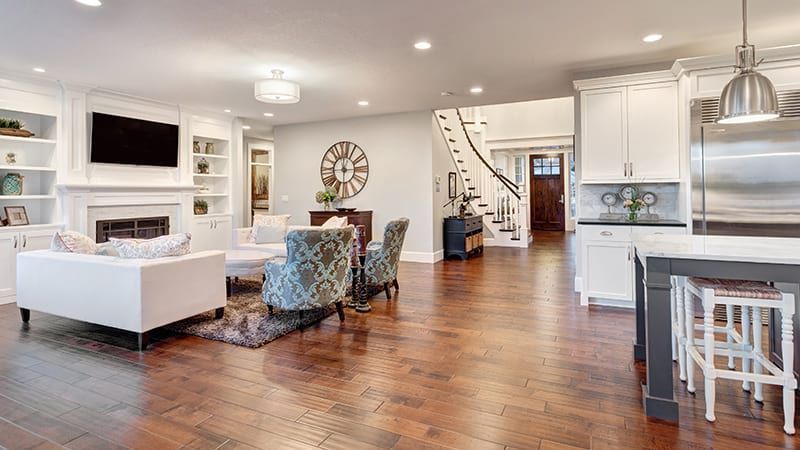 Spacious living room with white cabinets, hardwood floors, fireplace, staircase and kitchen island.
