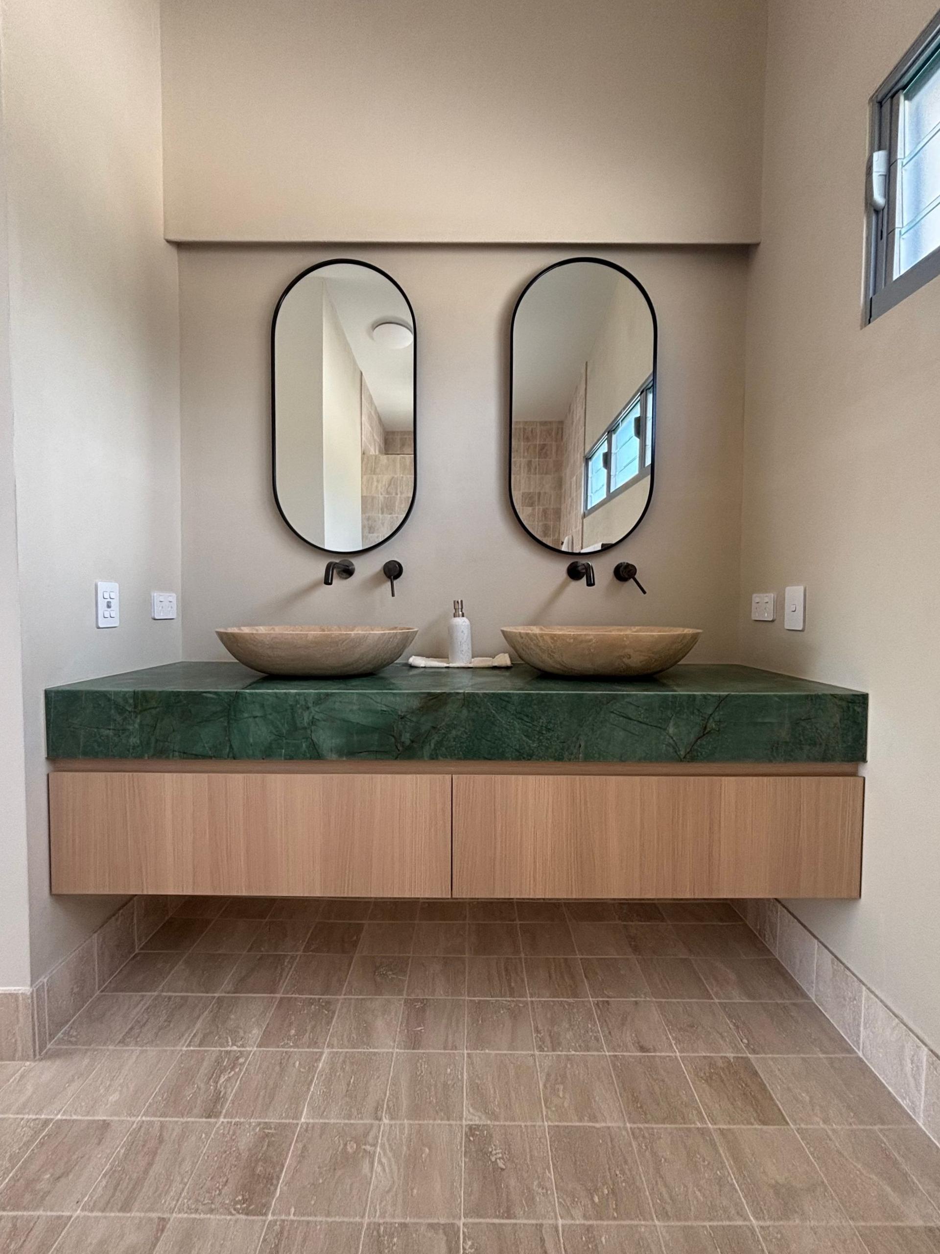 Modern bathroom with green marble countertop, wood cabinets, oval mirrors, and vessel sinks — Maken Kitchens & Cabinets in Chinderah, NSW
