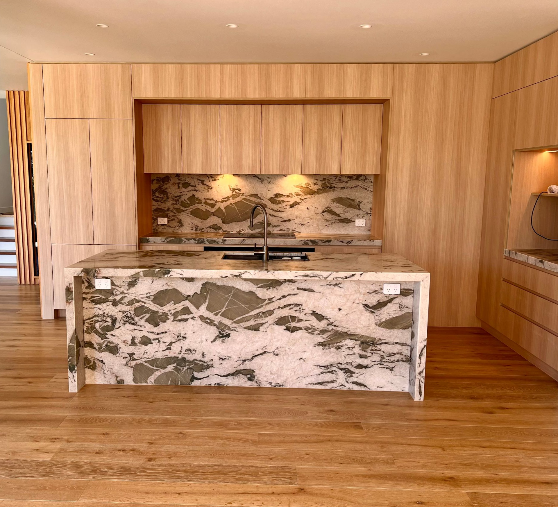 Modern kitchen with light wood cabinets, gray and white patterned island and countertops, and wood flooring — Maken Kitchens & Cabinets in Chinderah, NSW