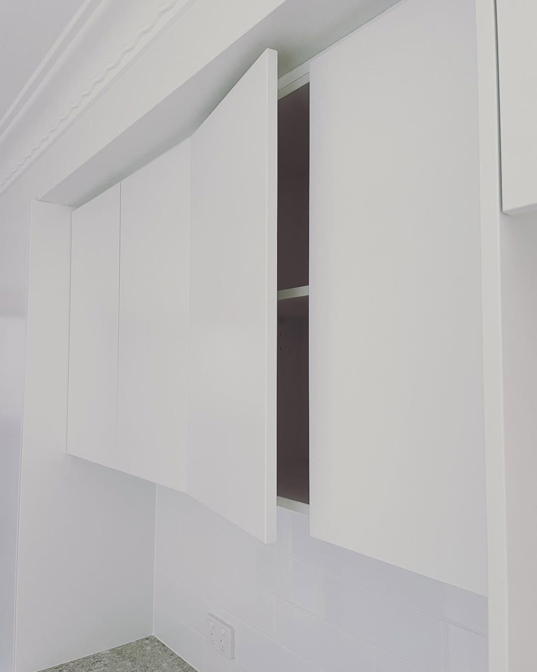 White kitchen cabinets, one open, revealing shelves against a brown interior. — Maken Kitchens & Cabinets in Pottsville, NSW