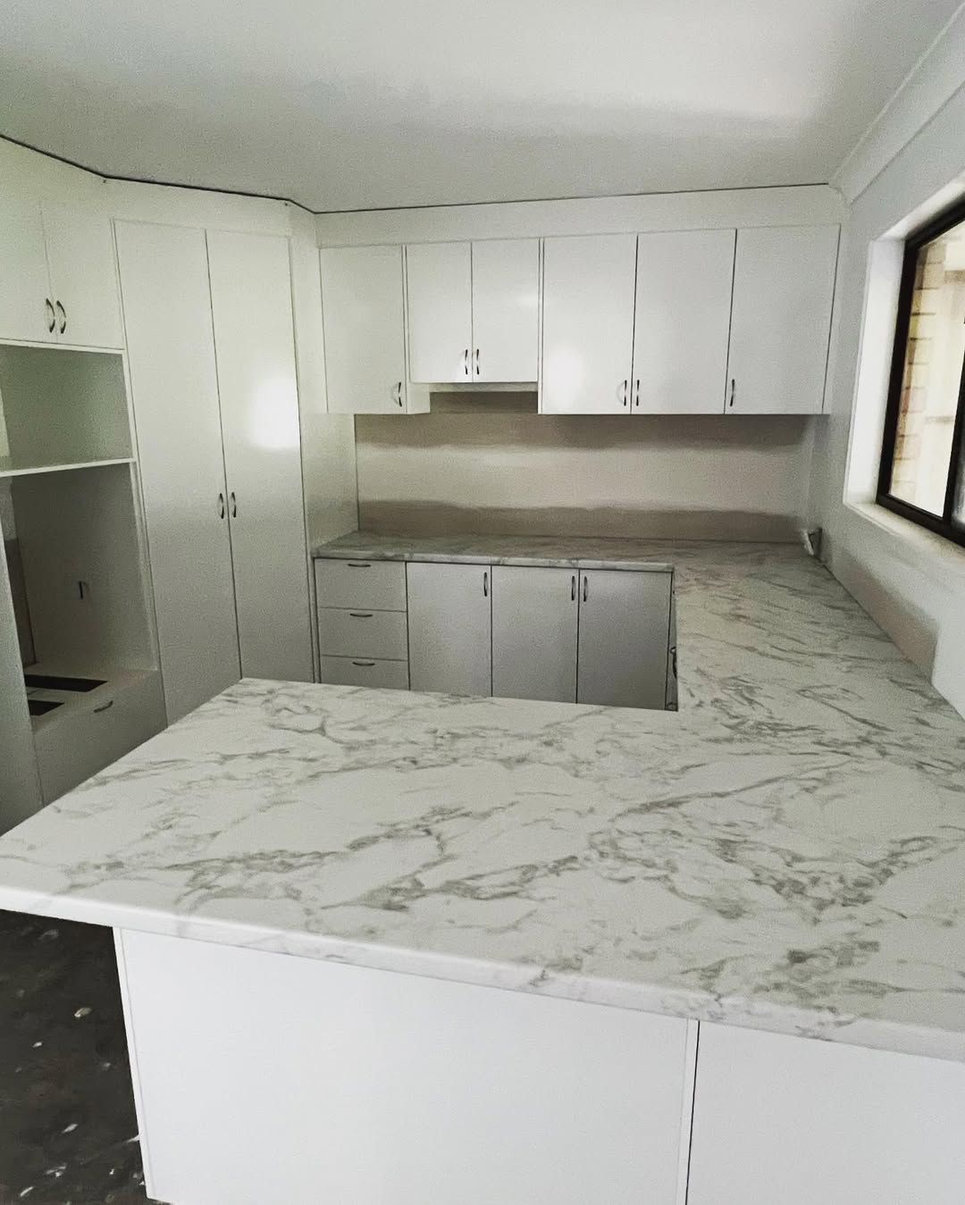 White kitchen cabinets and countertops with marble pattern, U-shaped layout, near a window. — Maken Kitchens & Cabinets in Tweed Heads, NSW