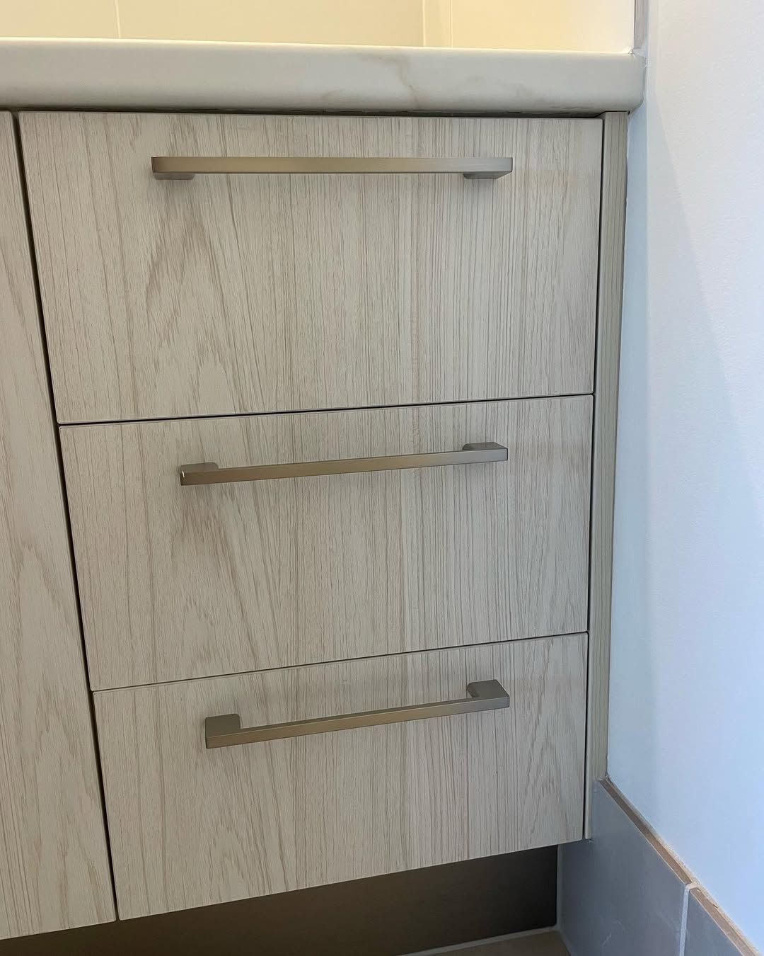 Three-drawer cabinet with brushed nickel handles, light wood grain texture, next to a white wall. — Maken Kitchens & Cabinets in Gold Coast, NSW