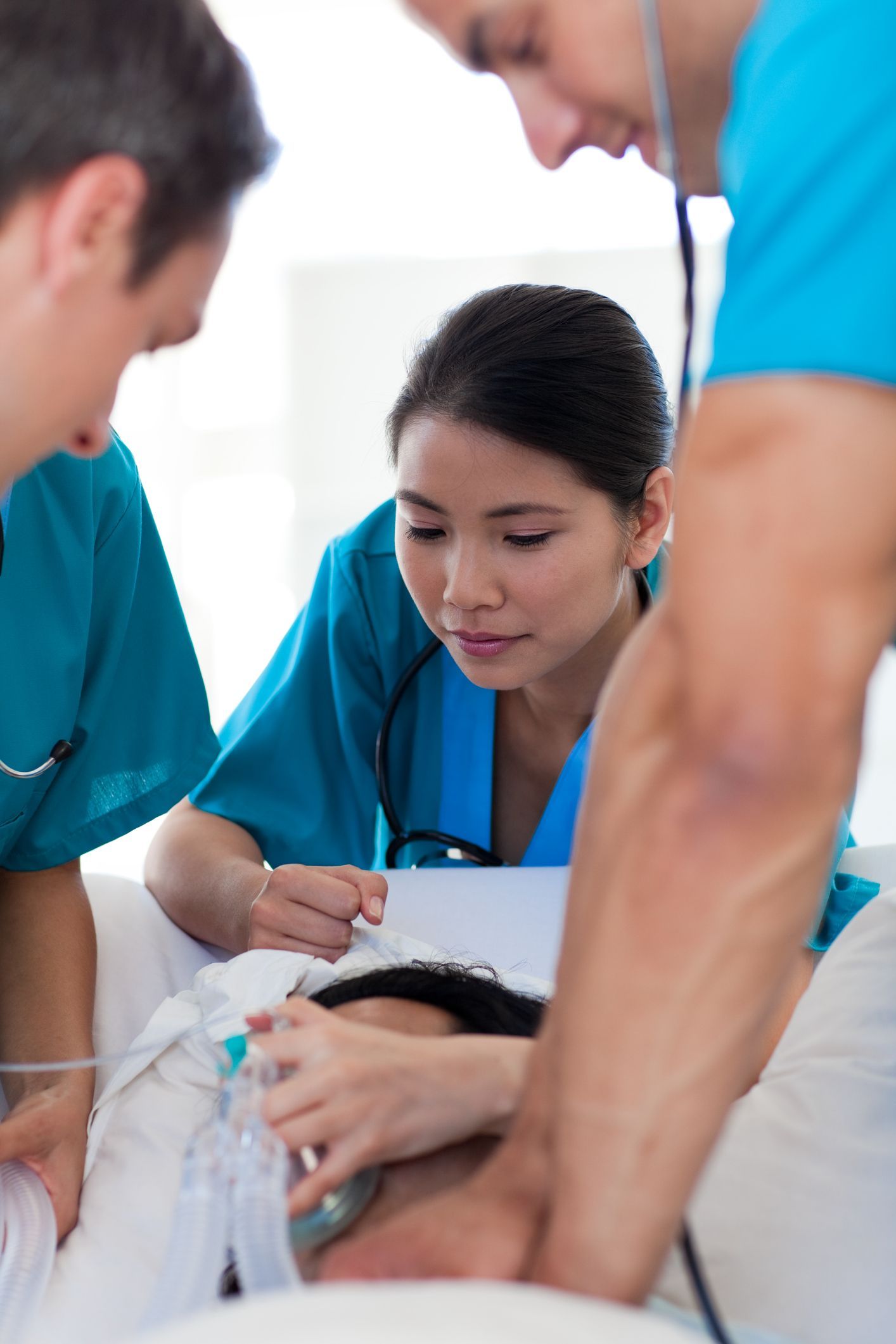 Team of 3 doctors does CPR urgent care on a patient in medical bed, with blurry white background. Team of 3 doctors does CPR urgent care on a patient in medical bed, with blurry white background.