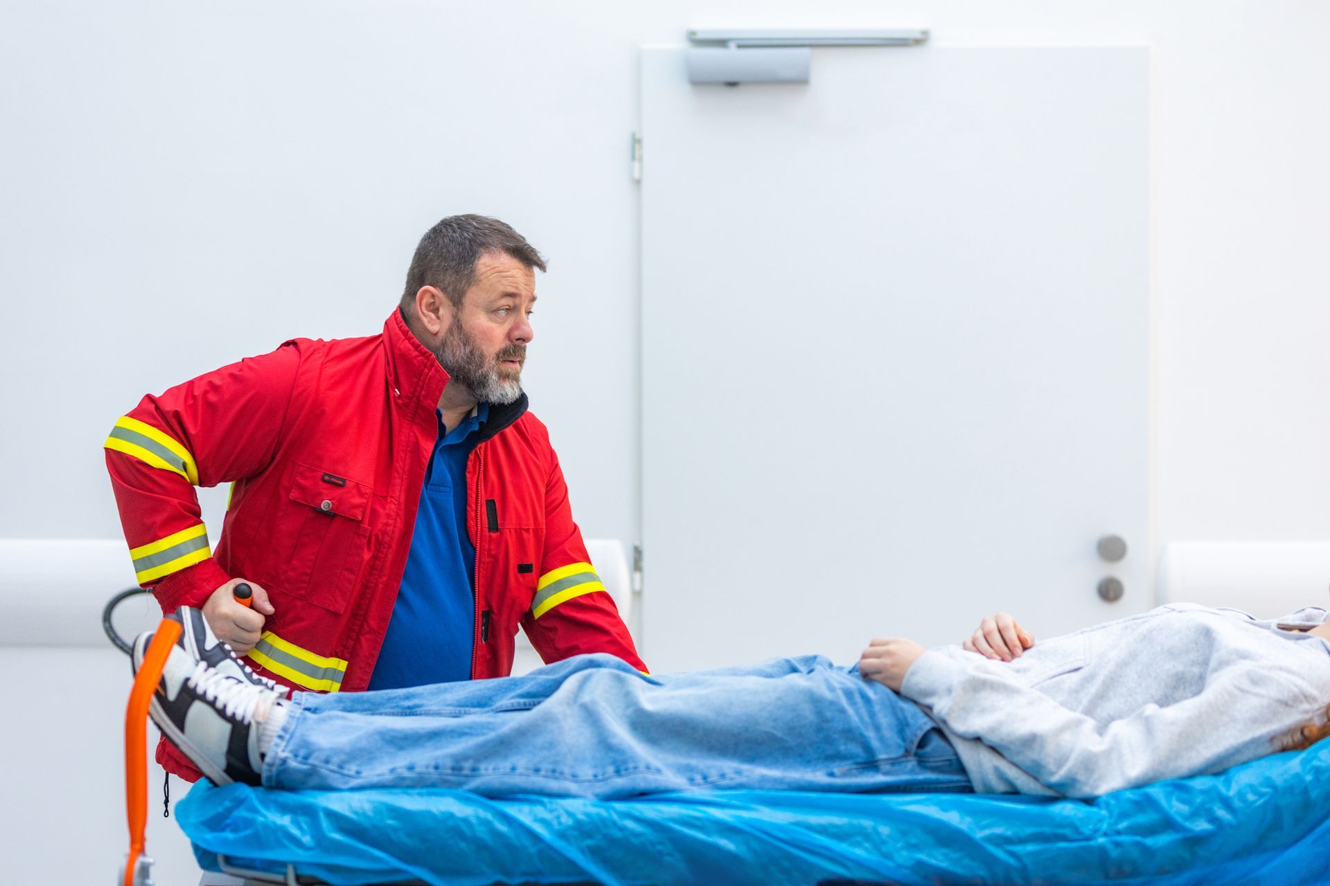 A man in a red jacket assists a woman on a stretcher, highlighting urgent care in action.