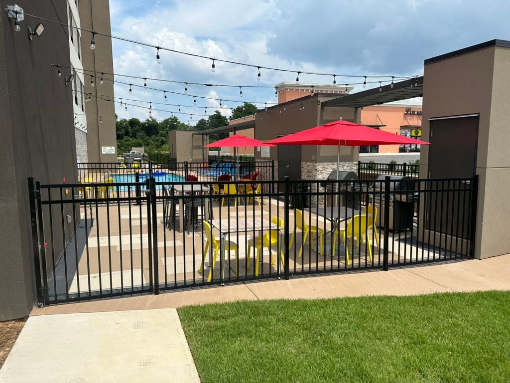Black fenced patio with yellow tables, red umbrellas, and string lights.