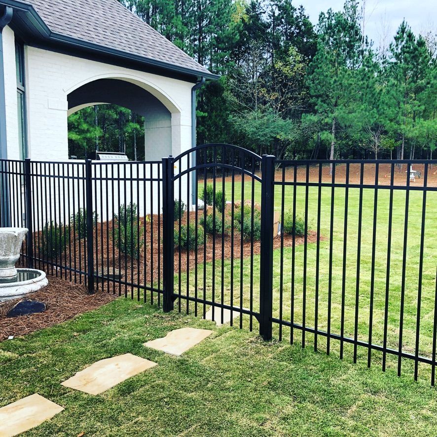 Black metal fence with gate in front of a white house with a lawn.