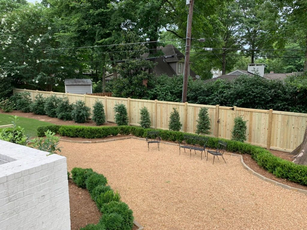 A wooden fence is surrounded by bushes and gravel in a backyard.